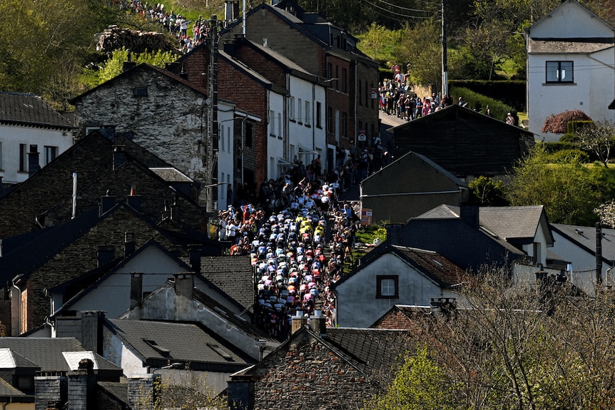 An overhead shot showing cyclists on a narrow road between old houses.