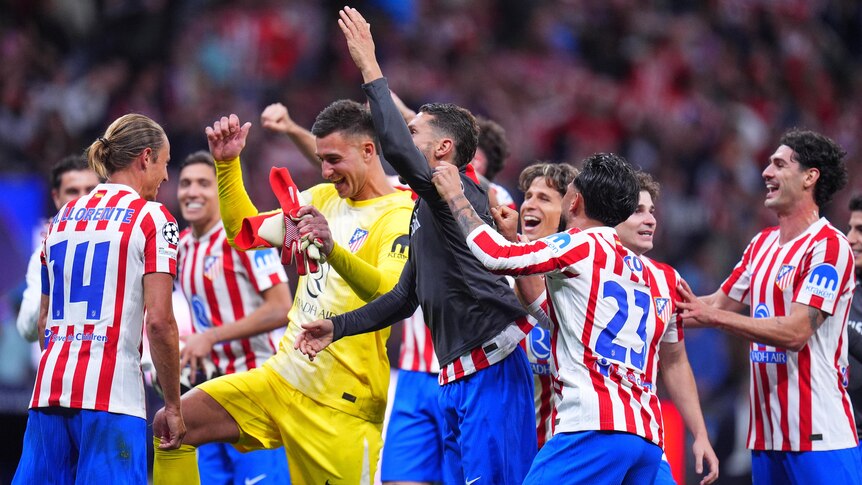 A group of Atlético Madrid soccer players grin and celebrate together after winning a Champions League knockout tie.