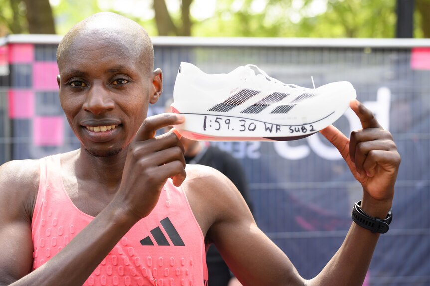 Sabastian Sawe holds up a shoe in his running gear
