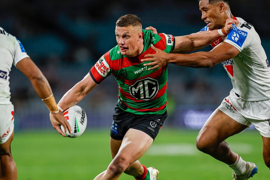 NRL player running with the ball, trying to offload while being tackled