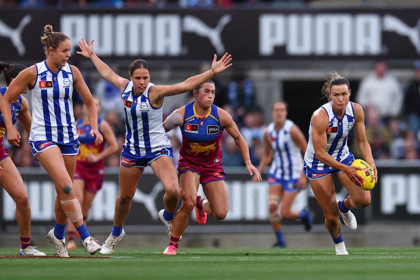 An AFLW player in white and blue carries the ball amid a group of players