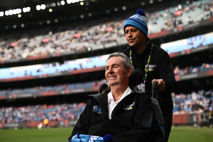 A man in a beanie steers a smiling man in a wheelchair. 
