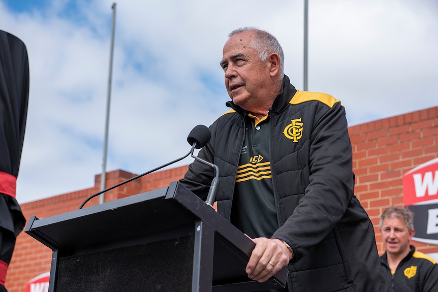 A man stands at a podium wearing black and gold