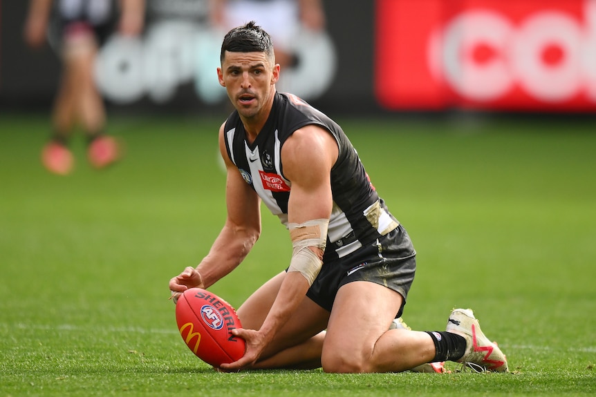 AFL player stoops to pick up a ball.