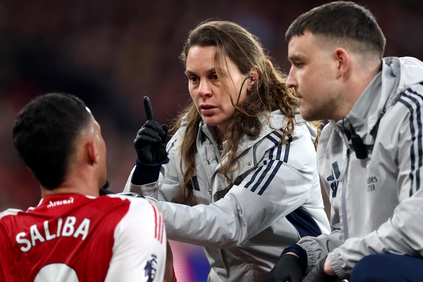 A club doctor points a finger in front of an Arsenal player to conduct a concussion test during a game.