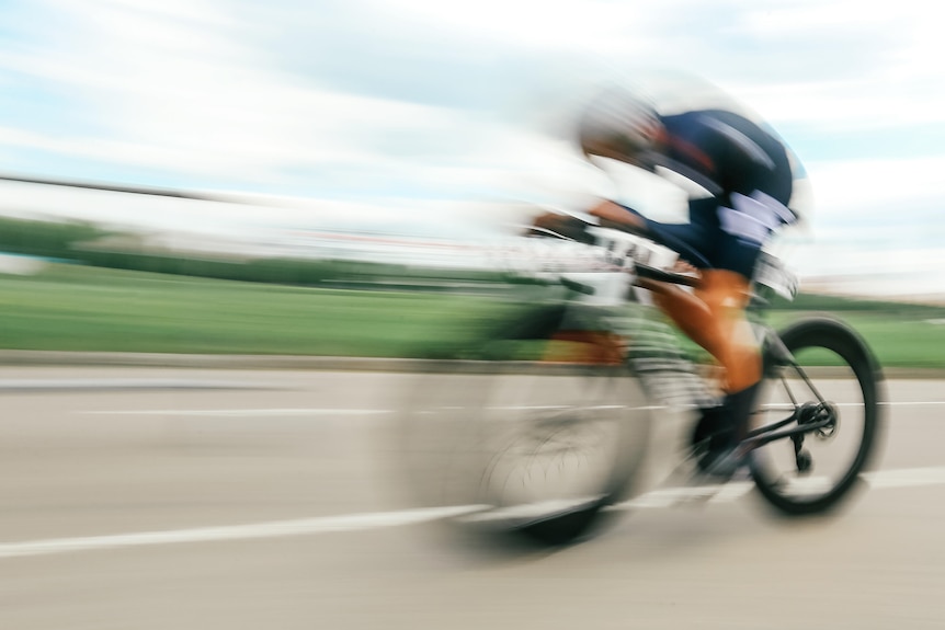 A cyclist pedals past the camera with a blur in the shot.