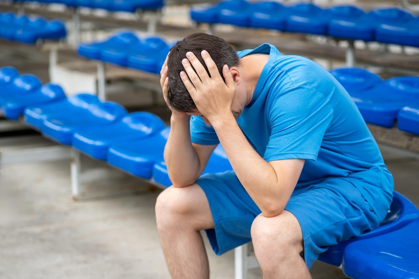 A man is sitting on a bench and has hands in head in pain.