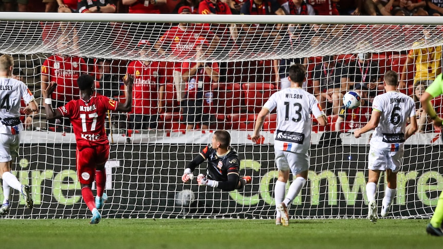 A picture from distance of an Adelaide United A-League player watching his shot go past the goalkeeper into the net.
