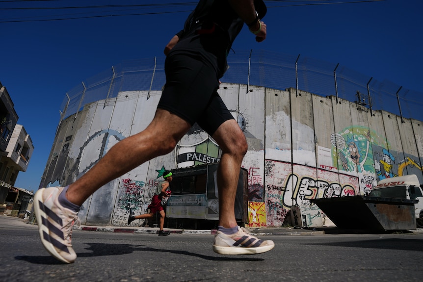Runners run past a wall