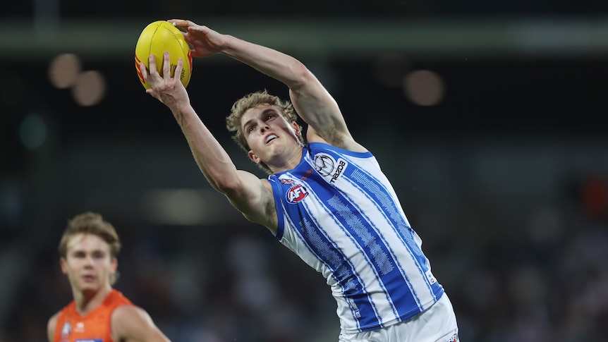 A North Melbourne AFL player reaches up and to his right to take an uncontested mark in a game against GWS.