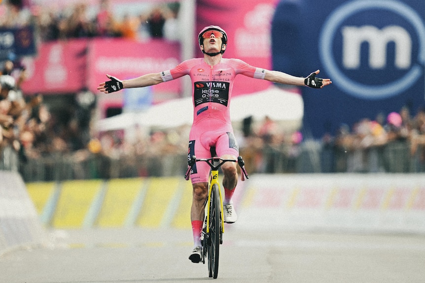 Jonas Vingegaard holds out his hands in victory while cycling. 