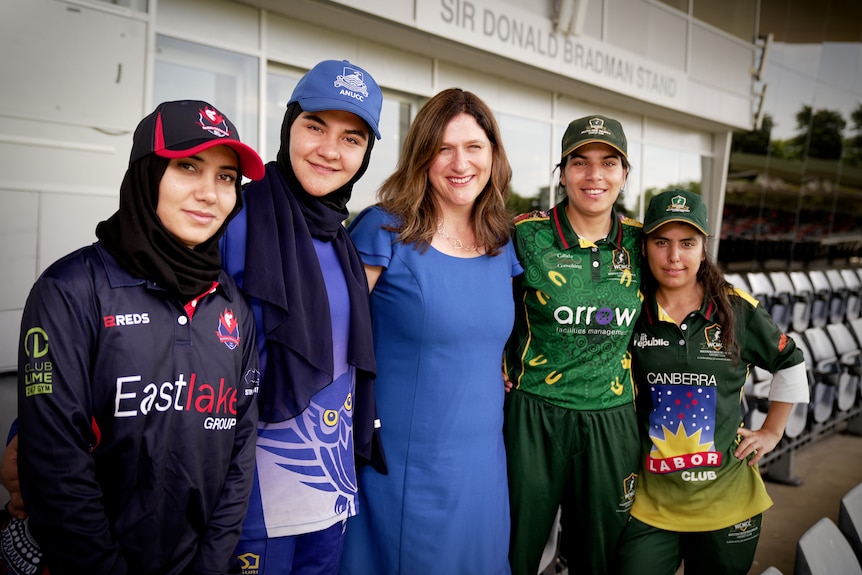 Women in cricket gear pose standing together at Manuka oval.