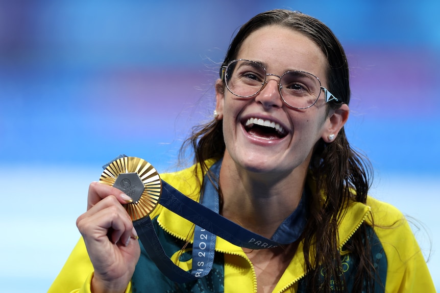 Kaylee McKeown smiles widely while holding her gold medal