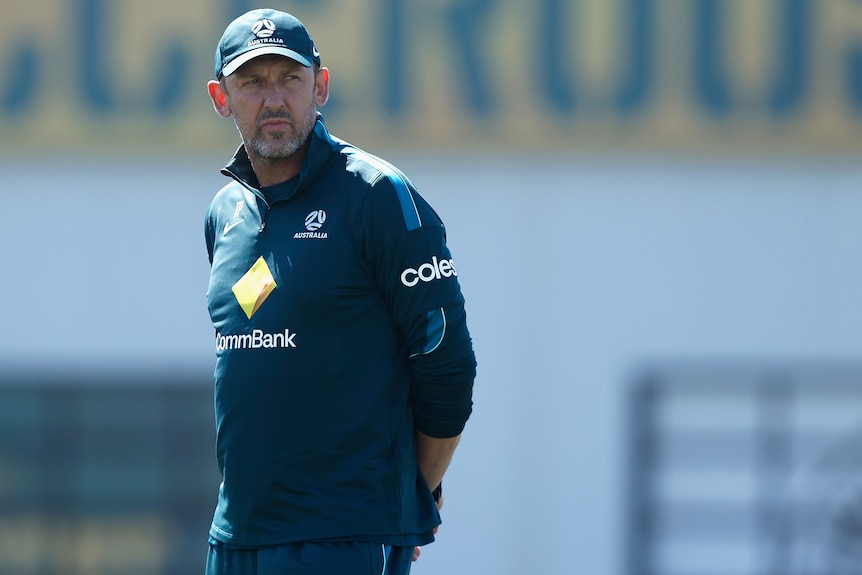Tony Popovic looks over his shoulder at Socceroos training, wears green jersey cap with coles, CBA labels.