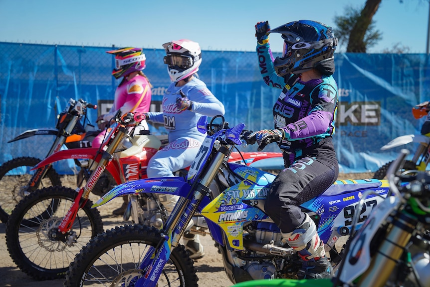 Three female motorbike riders at the start line of a bike racing event.