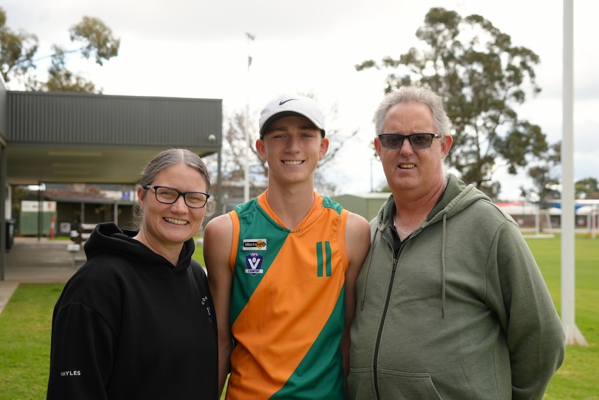 A young man in a Sunraysia geurnsey surrounded by his parents all smiling