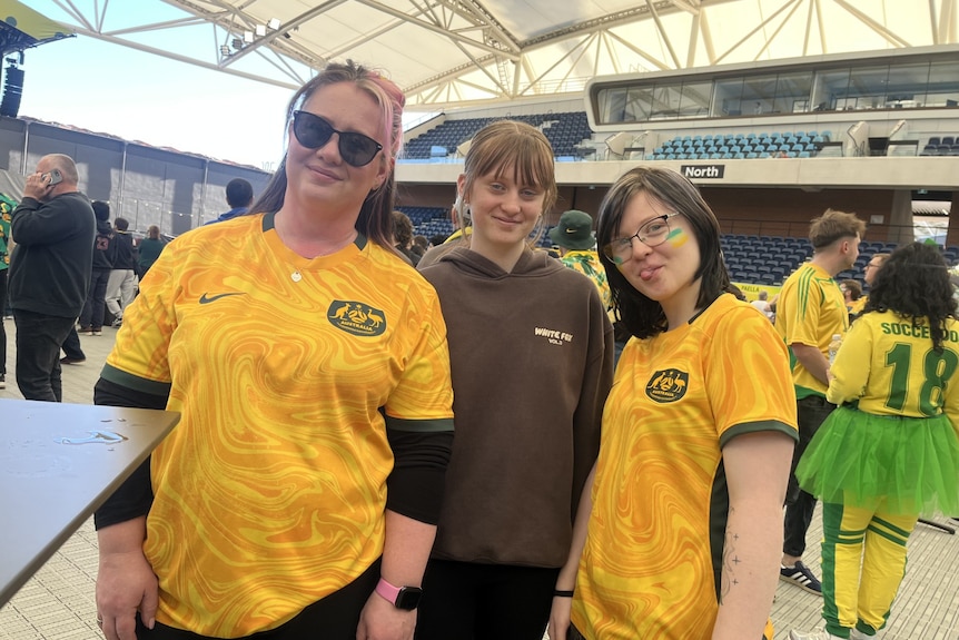 three women in Soceroos tops smile at the camera