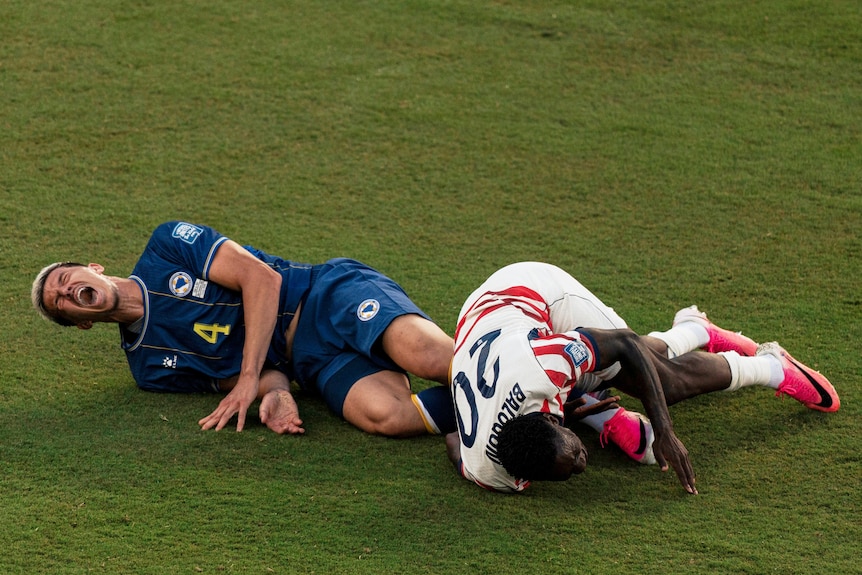 Folarin Balogun and Tarik Muharemović on the ground, both appearing to be in pain.