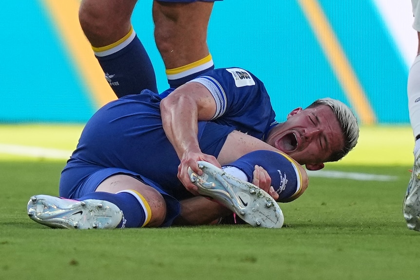 Tarik Muharemović screams, holding his foot while laying on the ground.