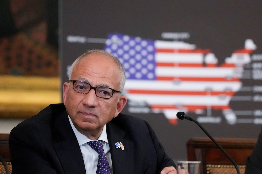Carlos Cordeiro sitting in front of a USA silhouette with a USA flag on it.