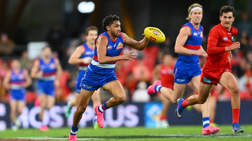 A Western Bulldogs player runs fast with the ball as a Gold Coast defender chases back.