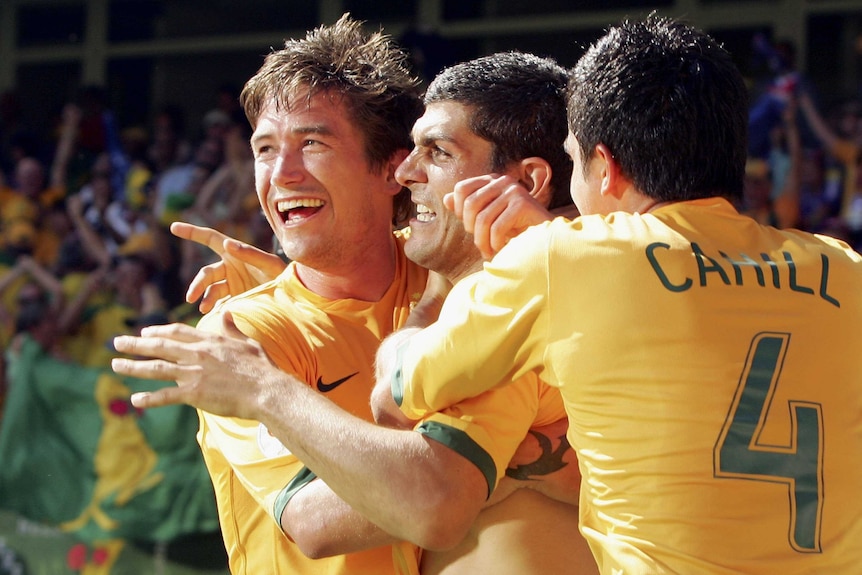 Three Socceroos throw their arms around each other in celebration.