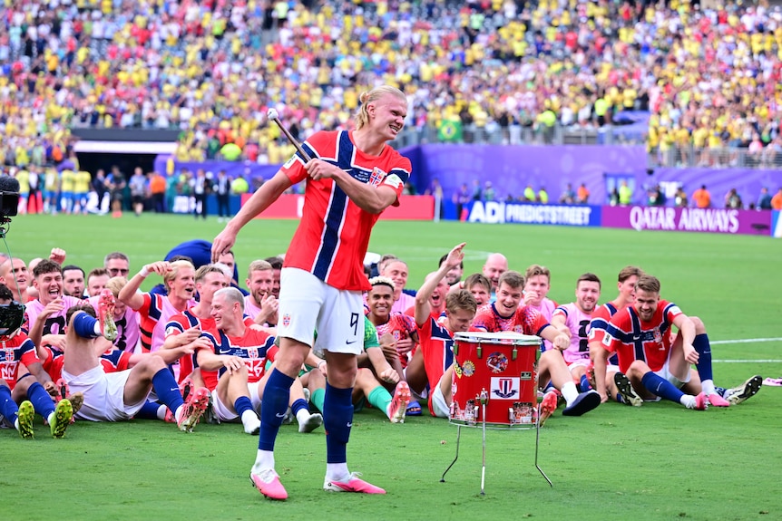 Erling Haaland bangs a drum with his teammates sitting down behind him to perform the viking row