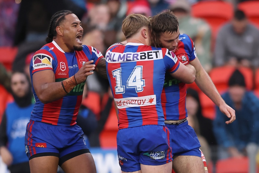 A group of rugby league players in red and blue stripes celebrate a win, hugging each other