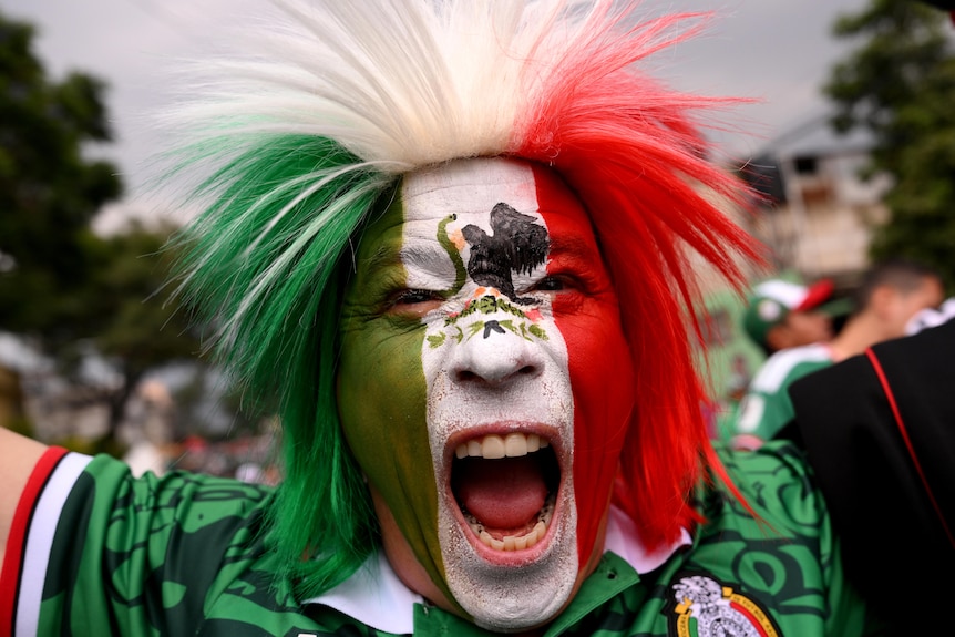 A Mexico fan roars while wearing facepaint and a coloured wig