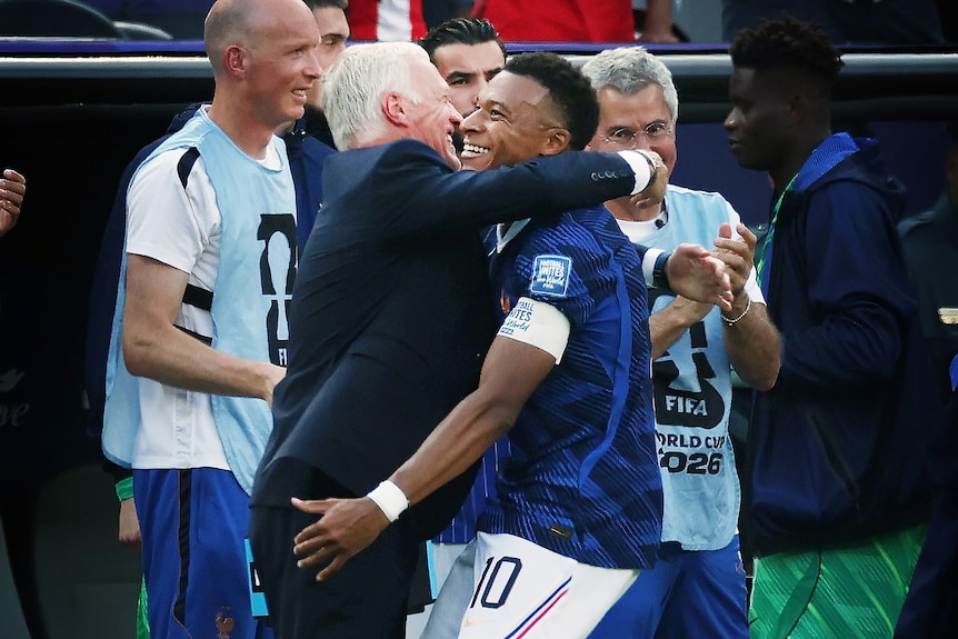 Didier Deschamps and Kylian Mbappe smile and hug on the touchline
