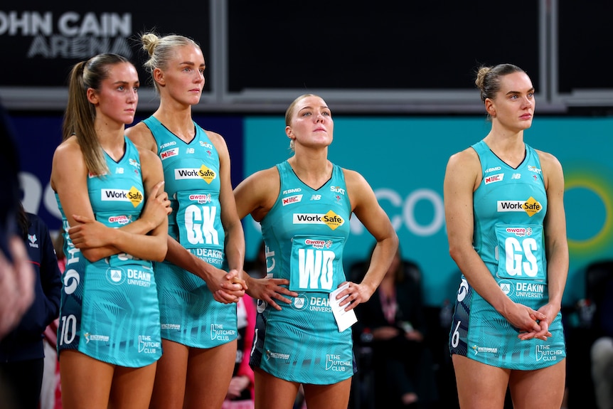 Four netball players stand beside each other looking sad and defeated.