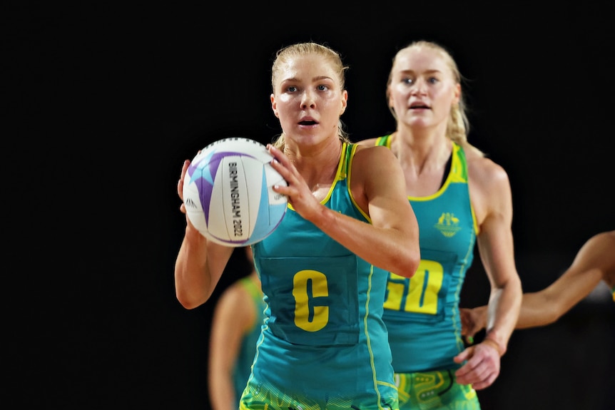 A female netballer holds the ball in front of her looking like she is about to pass.
