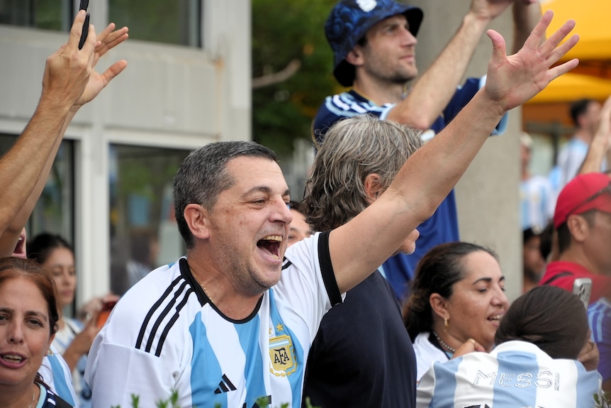 A man wearing an Argentina football jersey sings along to a song with arm outstretched