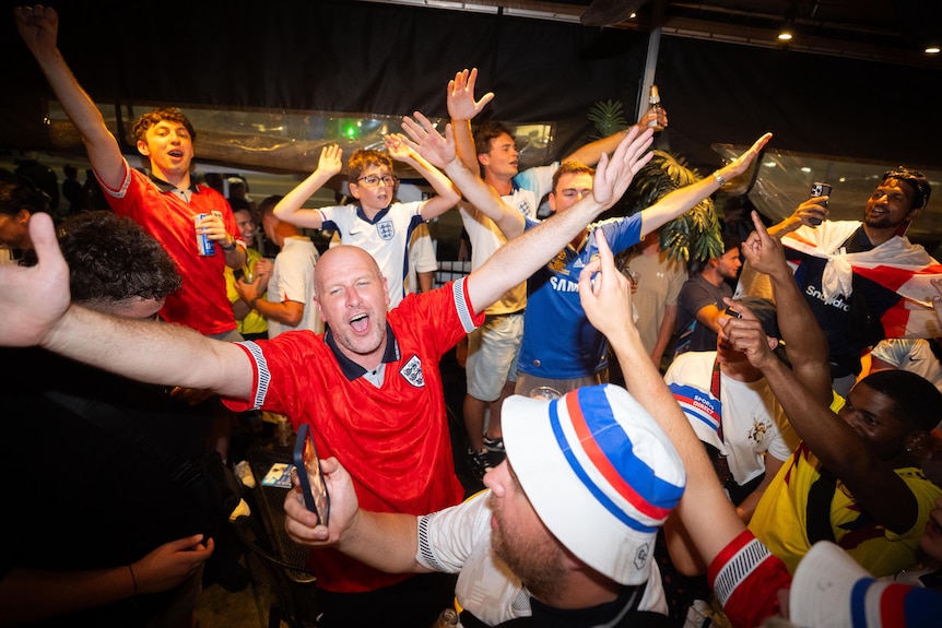 England fans have arms outstretched and sing exuberantly in a pub