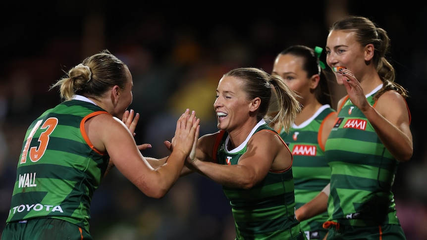 An Irish AFLW player smiles as her teammate high-fives her after a goal.