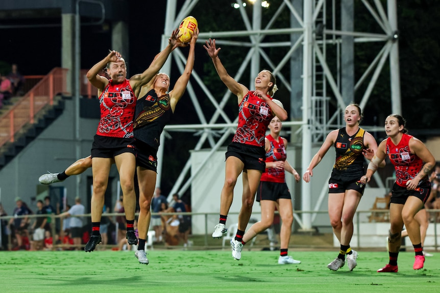 A group of players jump for a yellow AFL ball, two in red and one in yellow and black