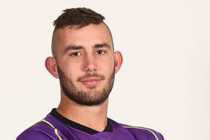 A sports headshot of a man in a purple uniform, smiling slightly.