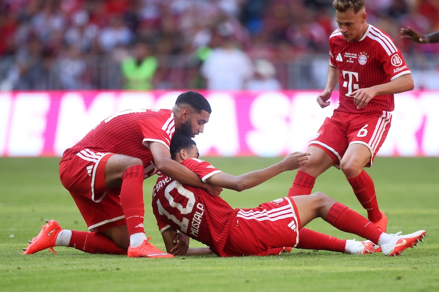 A man holds up another man as he falls to the ground during a football match.