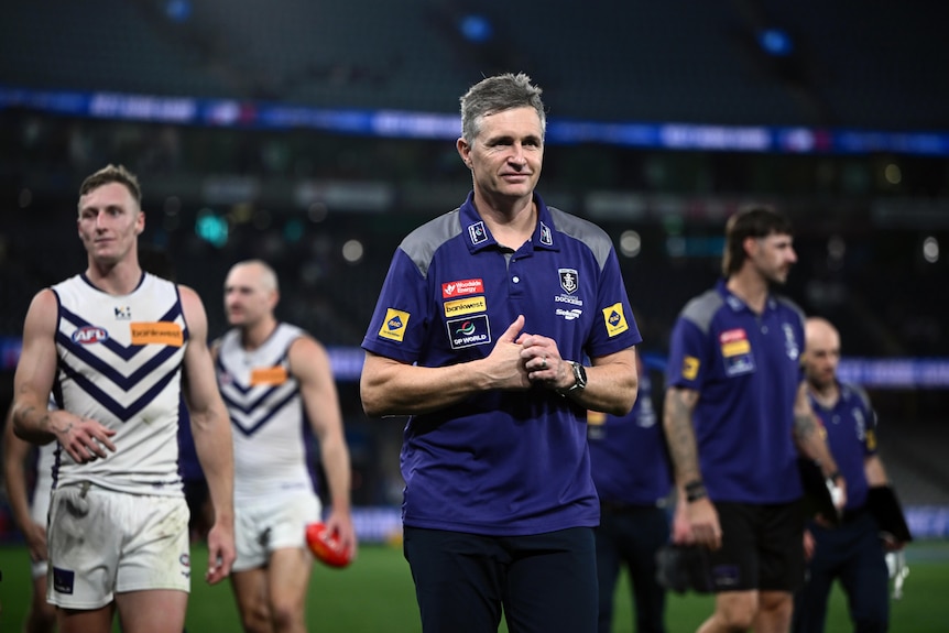 Justin Longmuir walks in a stadium with players behind him.