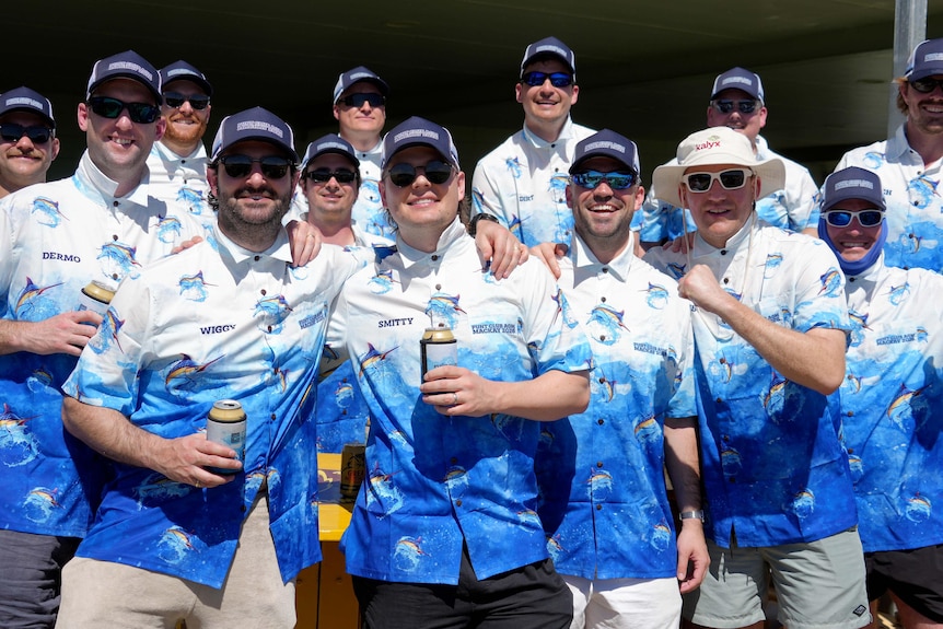 A large group of cricket male fans wearing matching shirts and holding cans of drink.