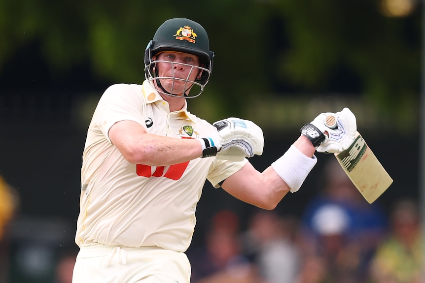A cricket batter plays a flat bat shot while looking uncomfortable