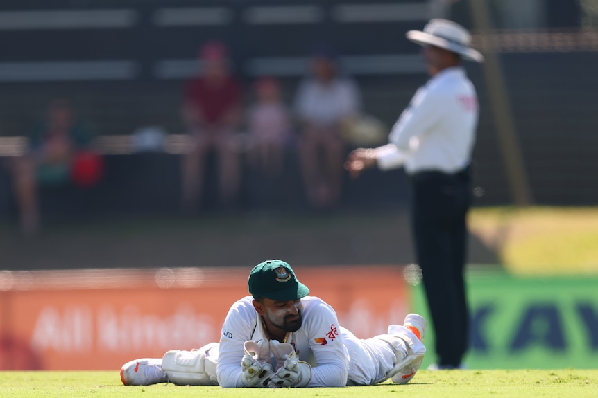 A cricketer is on the ground and outstretched with an umpire behind him