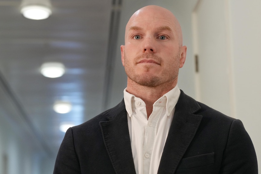 a young bald man wearing a suit in a hallway