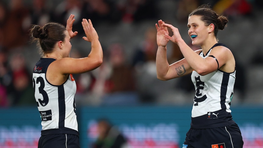 Two Carlton AFLW players clap hands in celebration after a goal by the player on the right.