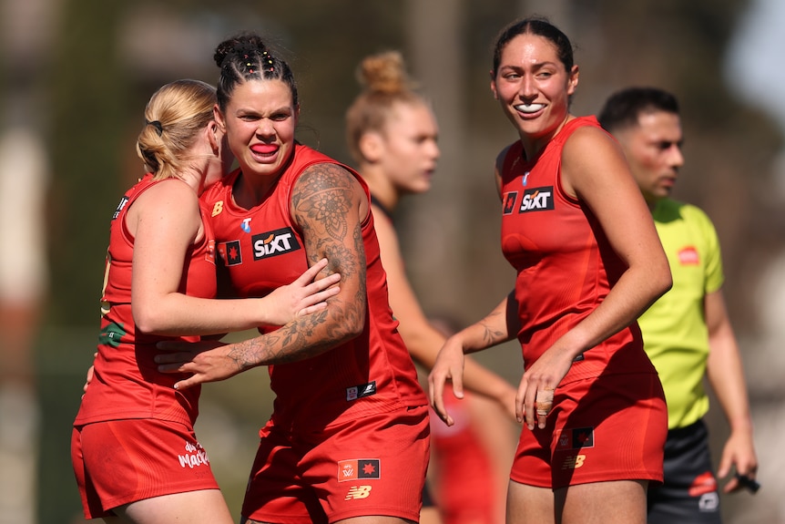 Three AFLW players in red celebrate a goal by hugging eachother