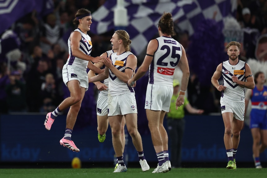 A group of AFL players in white celebrate a goal