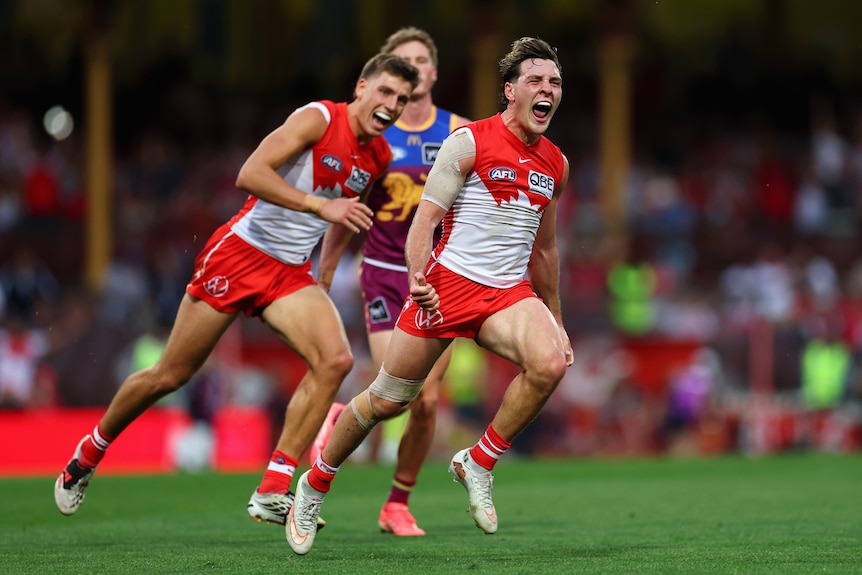 A Sydney Swans AFL player yells and runs away from his teammates after scoring a goal.