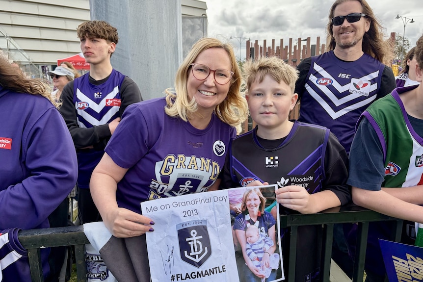 A woman with blonde hair and glasses smiles as she stands next to her son who holds a poster featuring the Dockers emblem