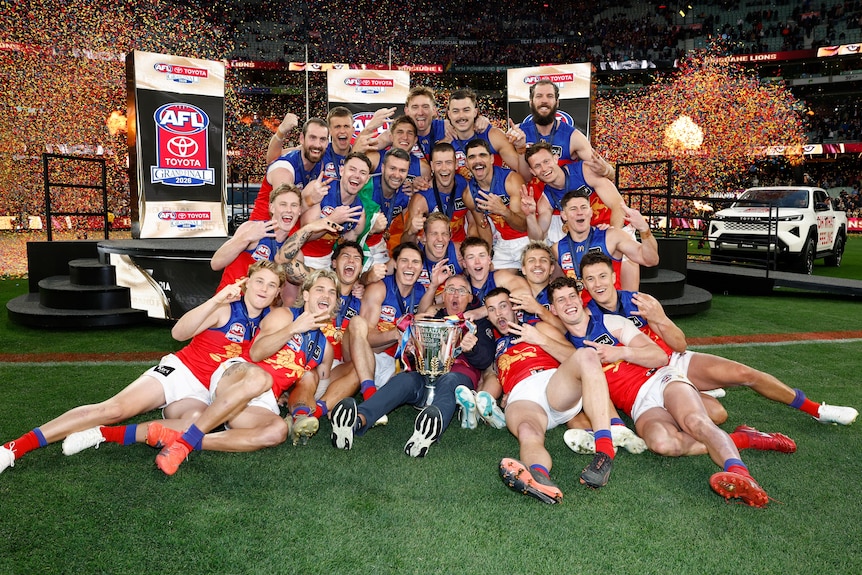 Lions players gather in rows for a celebratory photo, with medals around their necks, trophy in front and fireworks back