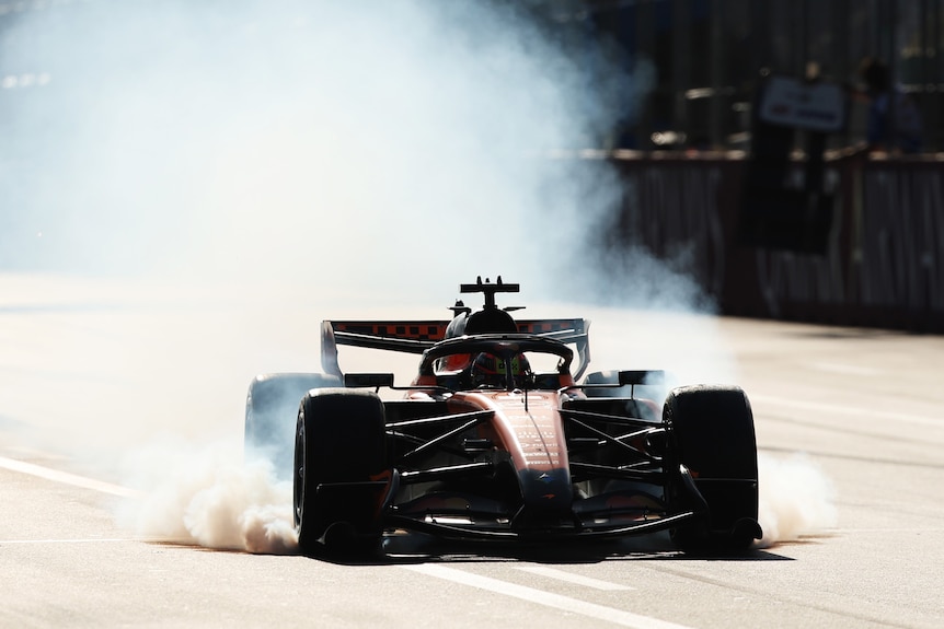 An F1 car has smoke coming from its back in sunshine